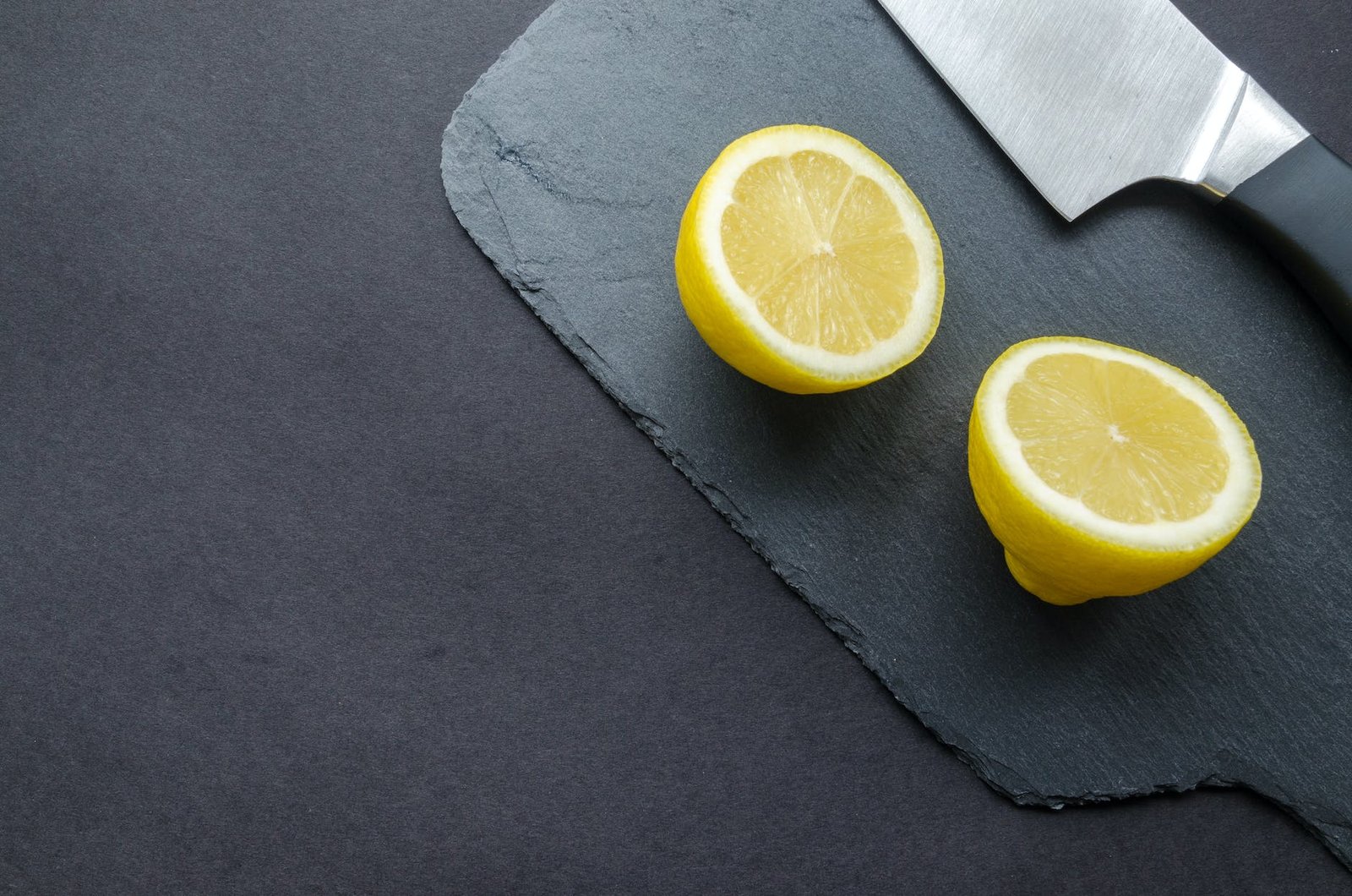 sliced lemon beside knife on top of black surface
